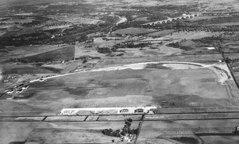 By 1930 the Minneapolis park board had begun the transformation of the old speedway into an airport, but a segment of the old 2-mile oval still remained. The Mendota Bridge is upper right. Note the NWA hangar among the airport buildings. The landing strip was not on the old concrete race track, which was too rough. The landing strip was on the grass in the infield of the old race track. (J. E. Quigley, Minneapolis Park and Recreation Board)